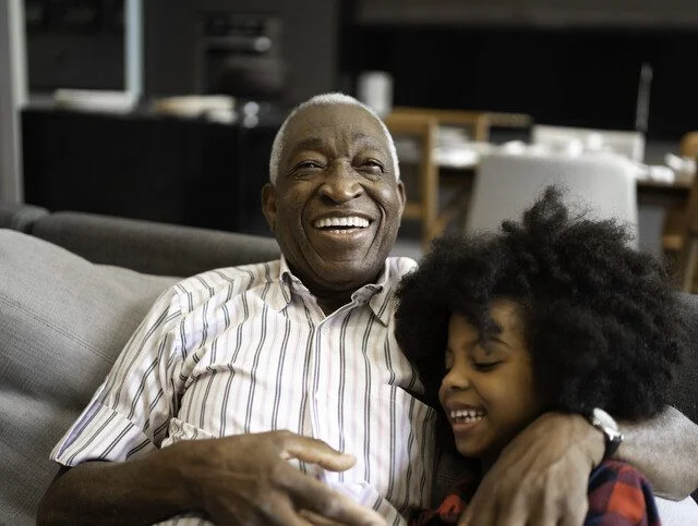 senior man sitting with his grandchild on the sofa smiling and laughing