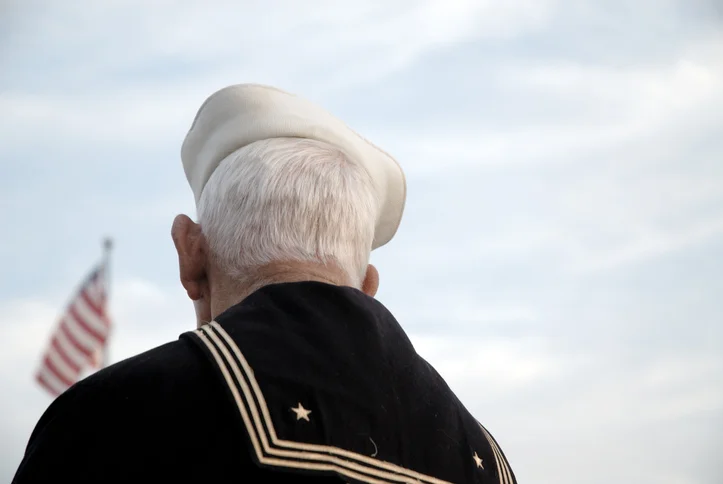Senior Navy Veteran gazes off into the distance at the American flag