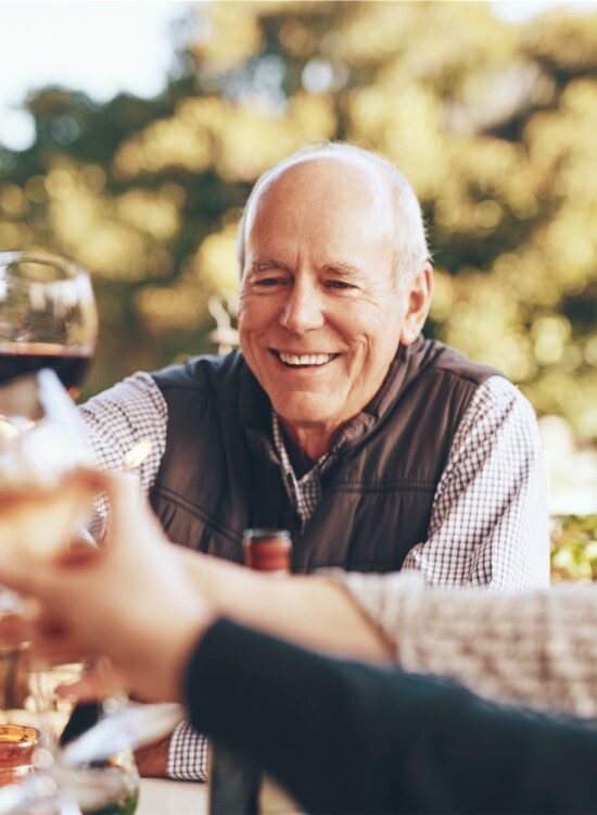 group of senior friends toast wine glasses together while dining outdoors