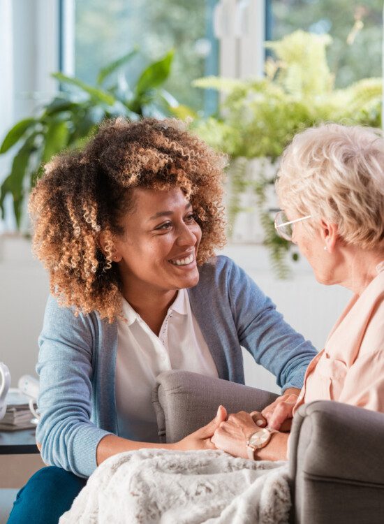 caregiver smiles while helping senior woman who sits in a reclining chair