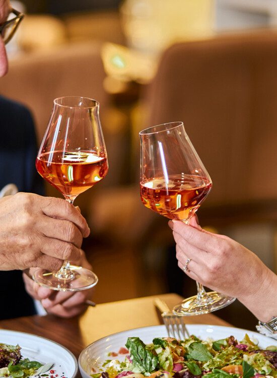 senior couple toasts glasses of wine together over an elegant, upscale meal