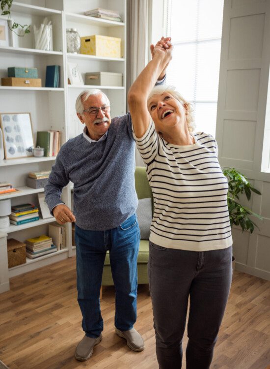 senior couple laugh and dance together in their apartment