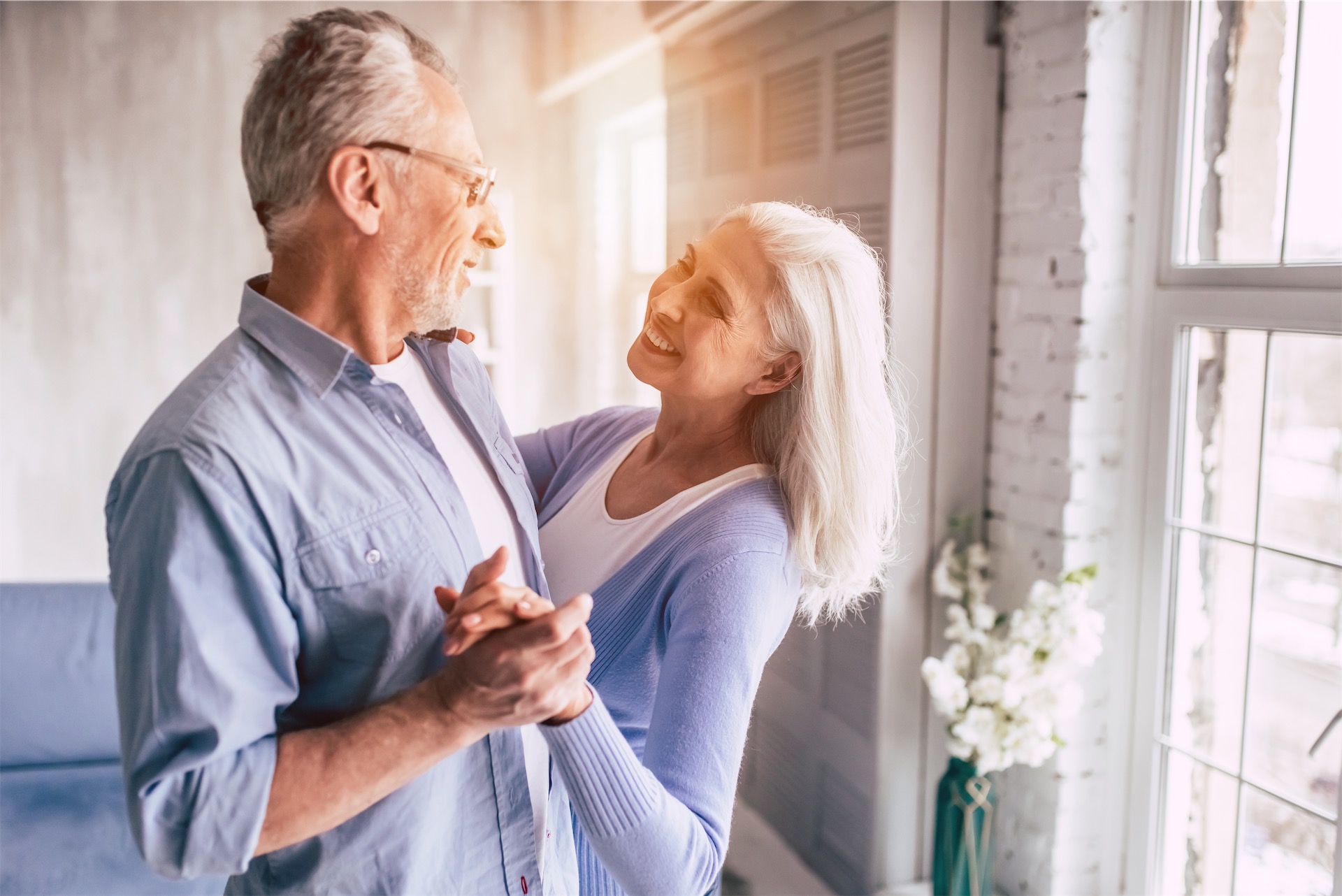 senior couple dances in their apartment, backdropped by sunlight