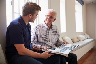 senior man and his adult son smile and look through an old photo album together