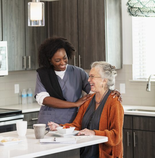 senior woman laughs while dining and speaking to her home caregiver