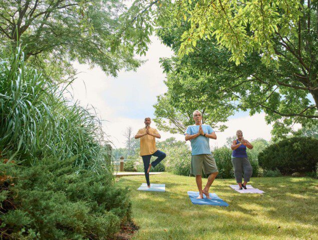 group of three seniors practice yoga poses outside at Oak Trace Senior Living Community