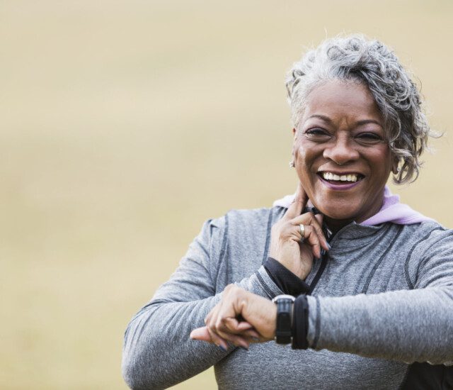 senior woman in athletic outfit smiles while checking her pulse after a walk