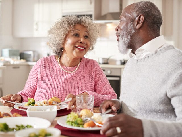 senior couple smile and enjoy a healthy dinner together in their apartment at Oak Trace Senior Living Community