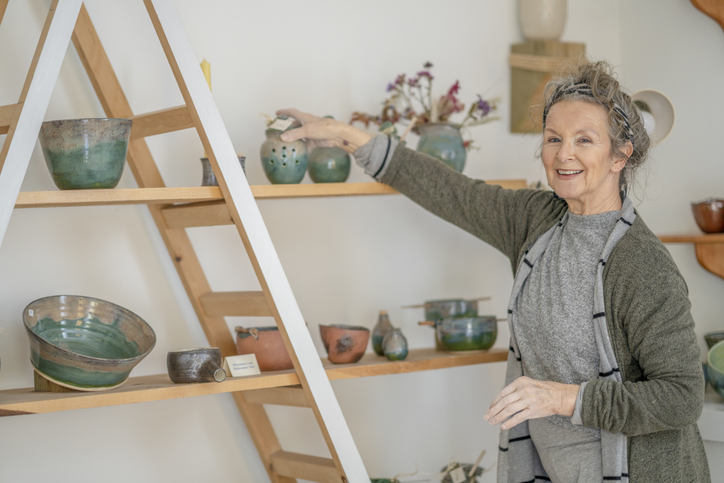 Senior woman smiles while placing pottery on a shelf