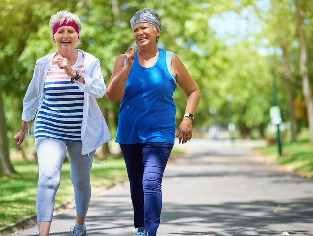 two senior women smile and talk while taking a brisk walk for exercise outside at Oak Trace Senior Living Community