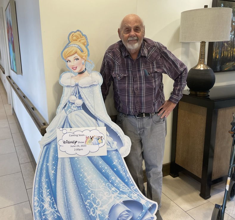 George Hlava, an Oak Trace Senior Living Community resident, smiles while posing next to a cut-out image of Cinderella