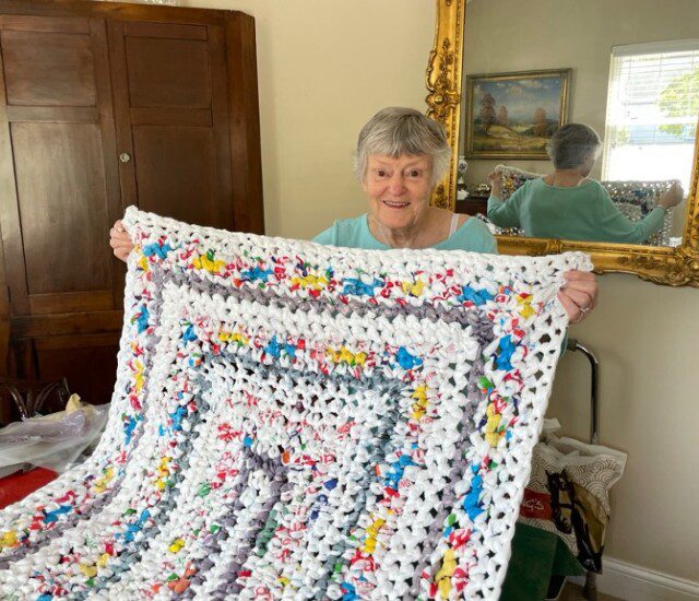 Senior woman smiles while showcasing a sleeping mat for the homeless she created using recycled grocery bags