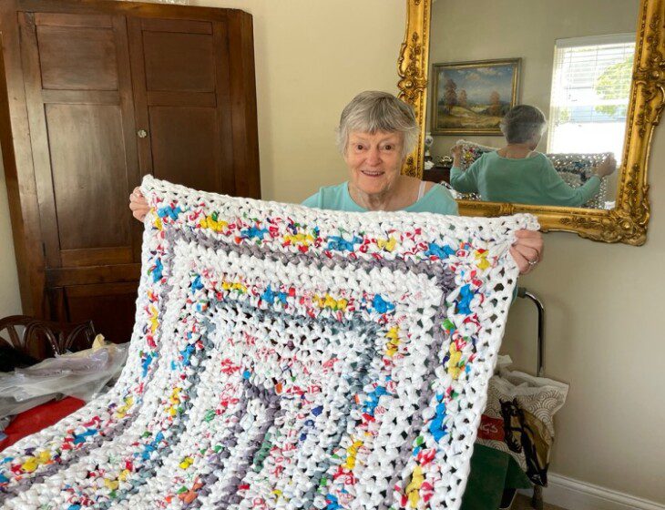 Senior woman smiles while showcasing a sleeping mat for the homeless she created using recycled grocery bags