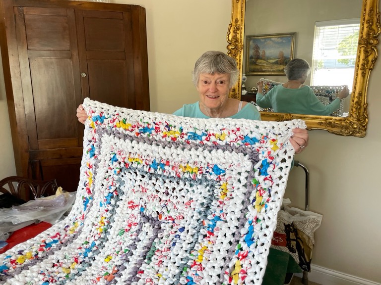 Senior woman smiles while showcasing a sleeping mat for the homeless she created using recycled grocery bags