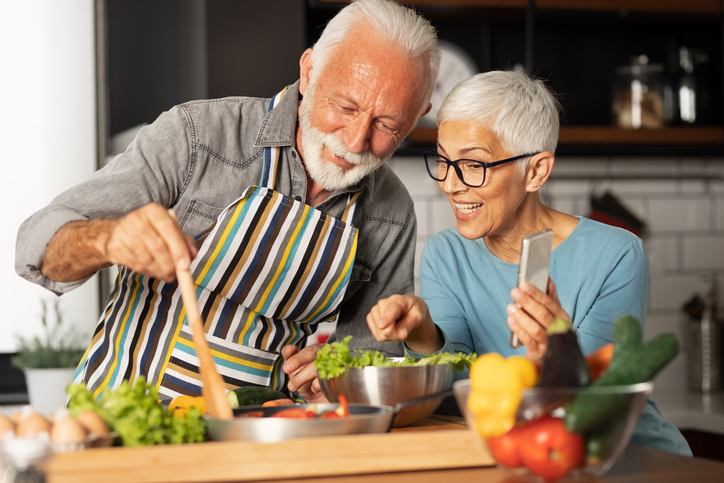 Senior couple smiles and cooks new recipe together in the kitchen