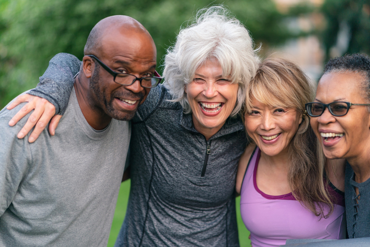 group of four seniors in athletic clothing smile and wrap their arms together